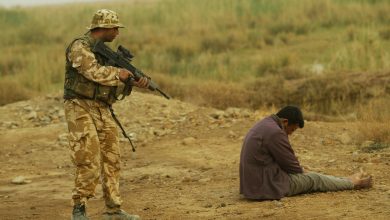 A British Royal Marines soldier stands guards over a Baath Party member, Southeast Basra, Iraq, 26 March 2003. PA Images via Reuters.