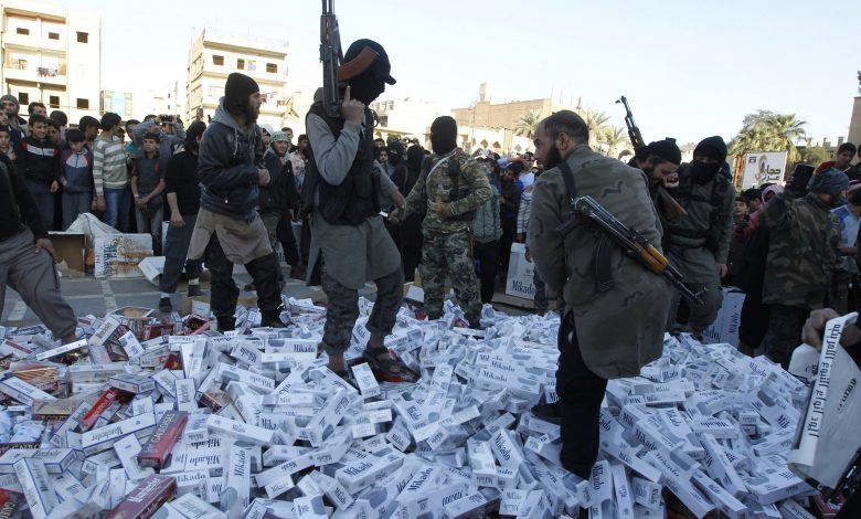 مقاتلون من تنظيم الدولة الإسلامية يحملون أسلحتهم ويقفون على عبوات سجائر مصادرة قبل حرقها، الرقة، سوريا، 2 أبريل 2014. رويترز، صحفي محلي.